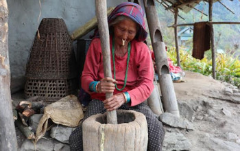 ओखलमा धान कुट्दै खाँदबारीकी वृद्धा