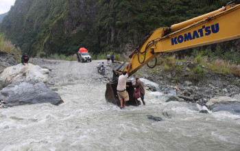 स्काभेटरको बकेटमा बसेर खोला तर्दै स्थानीय